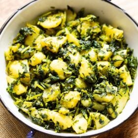 aloo methi in a enameled black rimmed small white wok on a brown jute napkin