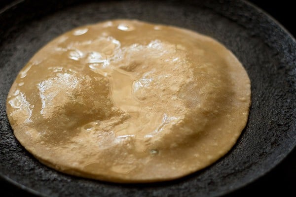 the aloo paratha has been brushed with oil and is beginning to puff up.