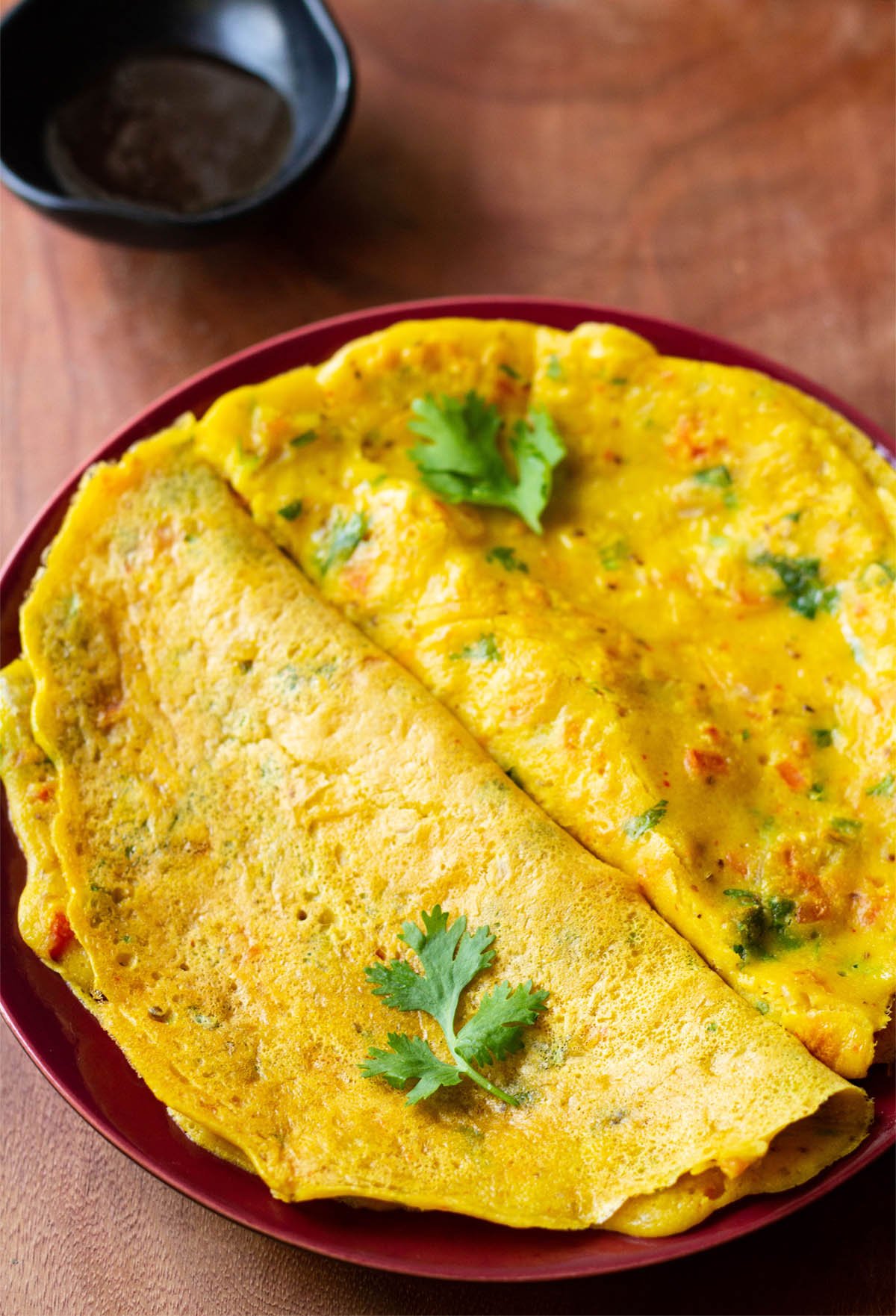 top shot of cooked and folded besan chillas on red plate with fresh herbs garnished on top