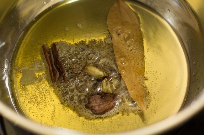 whole spices added to hot ghee in a pan for dum aloo recipe. 