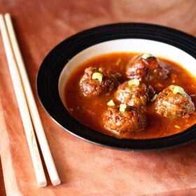 manchurian gravy garnished with chopped spring onion greens and served in a black rimmed bowl with chopsticks kept on the left side.