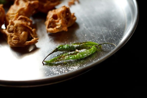 salt sprinkled on fried green chilies on a plate. 