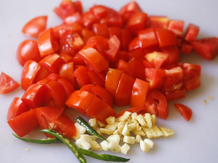 tomatoes, green chillies, ginger, garlic chopped on a white board
