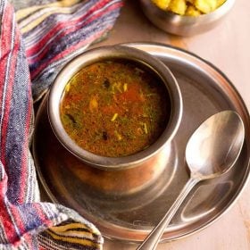 jeera milagu rasam served in a steel bowl with a spoon kept on the right side.