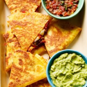 quesadilla triangles served in a tray with a side of guacamole and salsa.