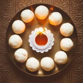 rava laddu in a circle with lit earthern lamp in center on a bronze plate.