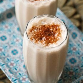 sharjah shake in 2 glasses sprinkled with bournvita on a blue design tray.