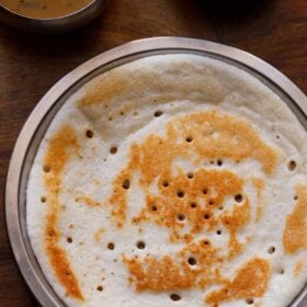 top shot of uttapam served on a steel plate with a side of coconut chutney and sambar.