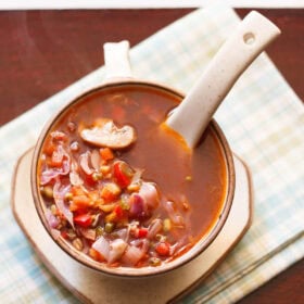 vegetable soup in a cream colored ceramic mug with a ceramic spoon inside the bowl on a checkered green, white, blue napkin.